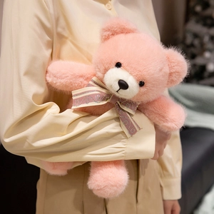 Pink teddy bear plush toy with ribbon bow being held in a cozy home setting