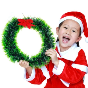 Classic green Christmas wreath with large red ribbon bow held by a child in Santa costume