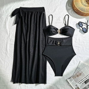Detail van een zwarte driedelige bikiniset met metalen ringen en transparante sarong