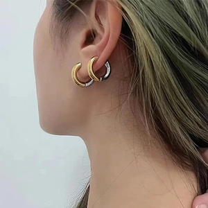 Close-up of dual-tone gold and silver C-shaped hoop earrings on a model earlobe