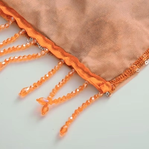 Close-up of orange translucent fabric featuring fringe tassels and acrylic beads