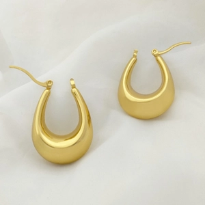 Detailed close-up of glossy gold U-shaped earrings on soft white textured fabric