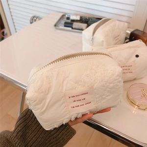 Détail d'une trousse à maquillage matelassée blanc cassé avec dentelle et étiquette
