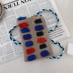 Detail of plush brown shoulder bag with colorful pompoms and a woven tricolor strap