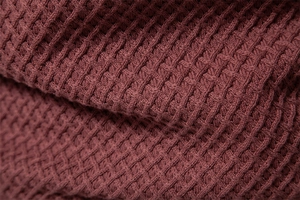 Macro shot of burgundy cotton knit fabric showing the detailed waffle texture on the sweater
