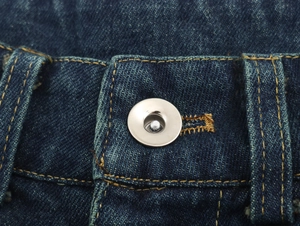 Gros plan du pantalon en jean bleu foncé avec bouton métallique et surpiqûres jaunes