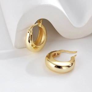 Macro shot of chunky gold hoop earrings on minimalist white textured stone backdrop