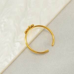 Détail macro d'une bague couronne dorée ajustable avec trois billes sur fond de marbre