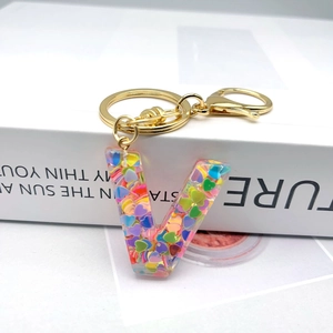 Macro detail of alphabet V resin keychain with colorful heart sequins and gold hardware