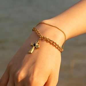 Detail of layered gold stainless steel cross bracelet with black gemstone on wrist