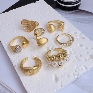 Set of 7 gold plated rings with heart diamond and pearl accents on white marble stone