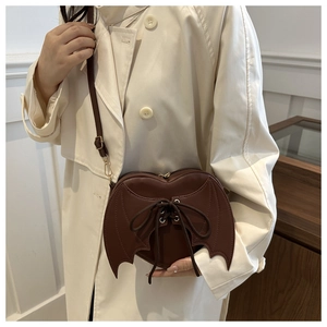 Model showing a brown heart-shaped bat wing crossbody bag with lace-up detail and PU leather