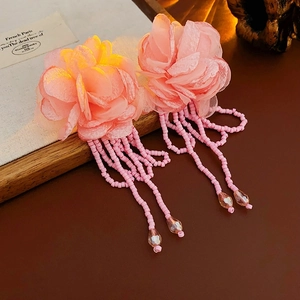 Detail of pink fabric flower earrings with beaded tassels on a wooden frame
