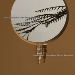 Detailed view of 18K gold-plated long fringe tassel earrings hanging on wooden frame