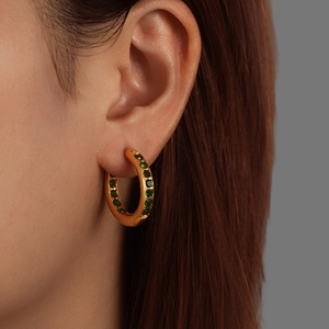 Elegant gold titanium earrings with green crystals worn by a model in a studio setting
