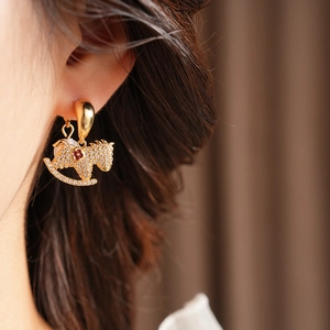 Macro shot of gold rocking horse earring with clear crystals and a red gemstone accent