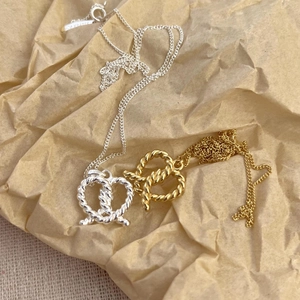 Macro detail of silver and gold pretzel bow necklaces showing S925 hallmark and logo