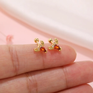 Detailed macro of a small gold crab stud earring with orange stone on a finger