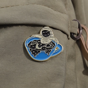 Creative astronaut in coffee cup enamel pin badge on a khaki canvas backpack strap