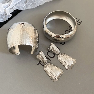 Detailed view of silver metal jewelry set including textured cuff and geometric earrings