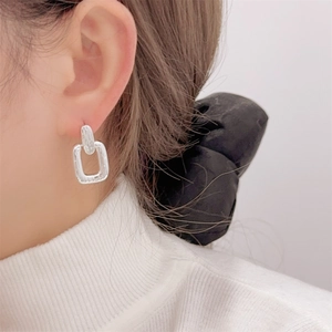 Macro shot of silver square geometric stud earrings worn on the ear for women