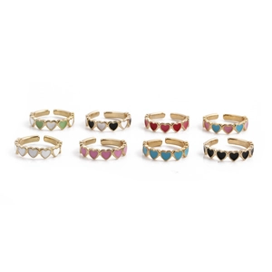 Close-up of eight colorful enamel heart rings in gold finish arranged on white background