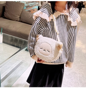 Detailed view of white plush lamb-shaped crossbody bag worn by child in cozy setting