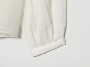 Detail of white long sleeve blouse showing pleated cuffs and striped chiffon texture