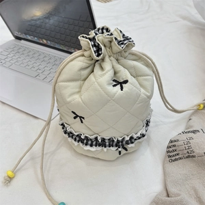 Close-up of quilted cream drawstring bag with black bow embroidery and checkered ruffle trim