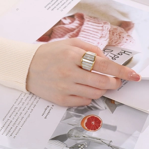 Detailed view of a wide gold-tone ring with inlaid white sea shells and linear textures