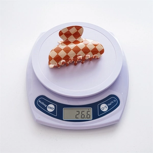Checkered hair claw clip in orange and beige on digital scale showing 26.6g weight