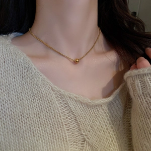 Detailed close-up of a minimalist gold bead pendant necklace worn on a woman's neck