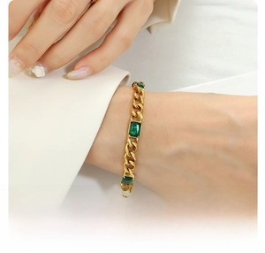 Makroaufnahme von 18k vergoldetem Titanstahl-Kettenarmband mit smaragdgrünen Steinen