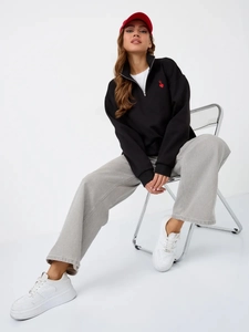 Detail of a black half-zip sweatshirt with a mini red heart logo on the chest