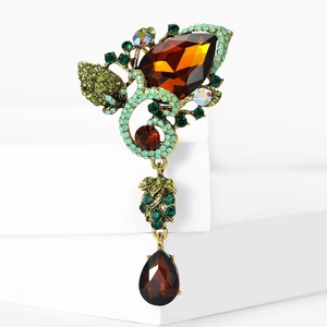 Macro detail of amber teardrop brooch with green rhinestones on gold base