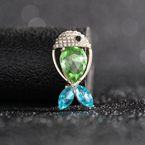 Macro shot of fish brooch featuring a large green pear-shaped stone and blue crystal tail