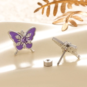 Silver titanium butterfly stud earrings with purple enamel and gemstones on beige background