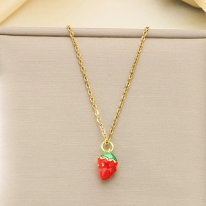 Macro view of a gold-plated necklace featuring a red enamel strawberry pendant on fabric