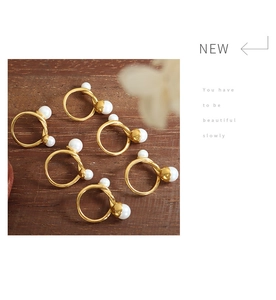 Detail shot of French style gold twisted rings featuring dual white pearls on wood surface