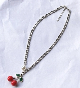 Detail of a silver chain necklace featuring a red cherry pendant and white pearl bead accent