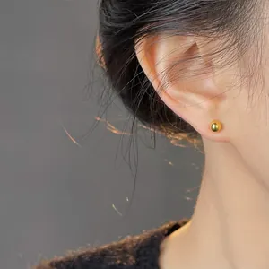 Close-up of minimalist polished gold ball stud earrings worn on earlobe for daily look