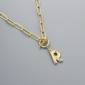 Detail of gold letter R pendant with trendy paperclip chain and decorative OT toggle clasp