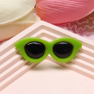 Detail of lime green resin miniature sunglasses accessory on pink textured display