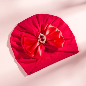 Detailed close-up of a red infant turban hat featuring a large satin bow and rhinestone