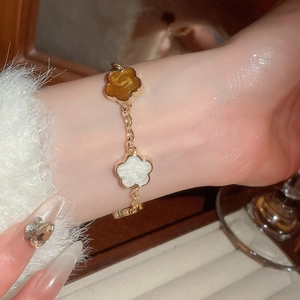 Gros plan d'un bracelet doré orné de breloques florales ambrées et blanc nacré au poignet