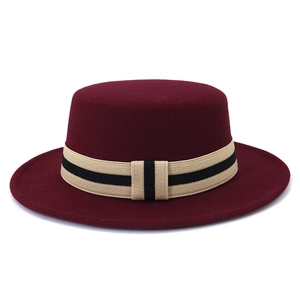 Detail of burgundy wool boater hat with a striped beige and black decorative band