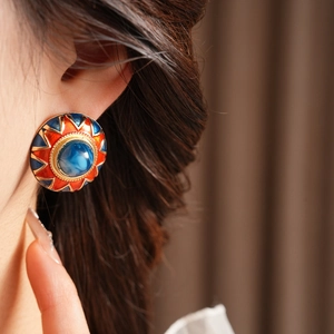 Detail of vintage round enamel earring with blue gemstone and gold serrated edge on ear