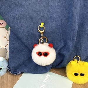Detail view of cute fuzzy plush ball keychains with sunglasses on denim bag