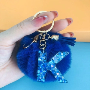 Detail of blue faux fur pompom and resin letter K keychain with gold hardware and tassel