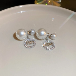 Detail of pearl earrings with micro-pave crystals and brand letter charm on ceramic tray